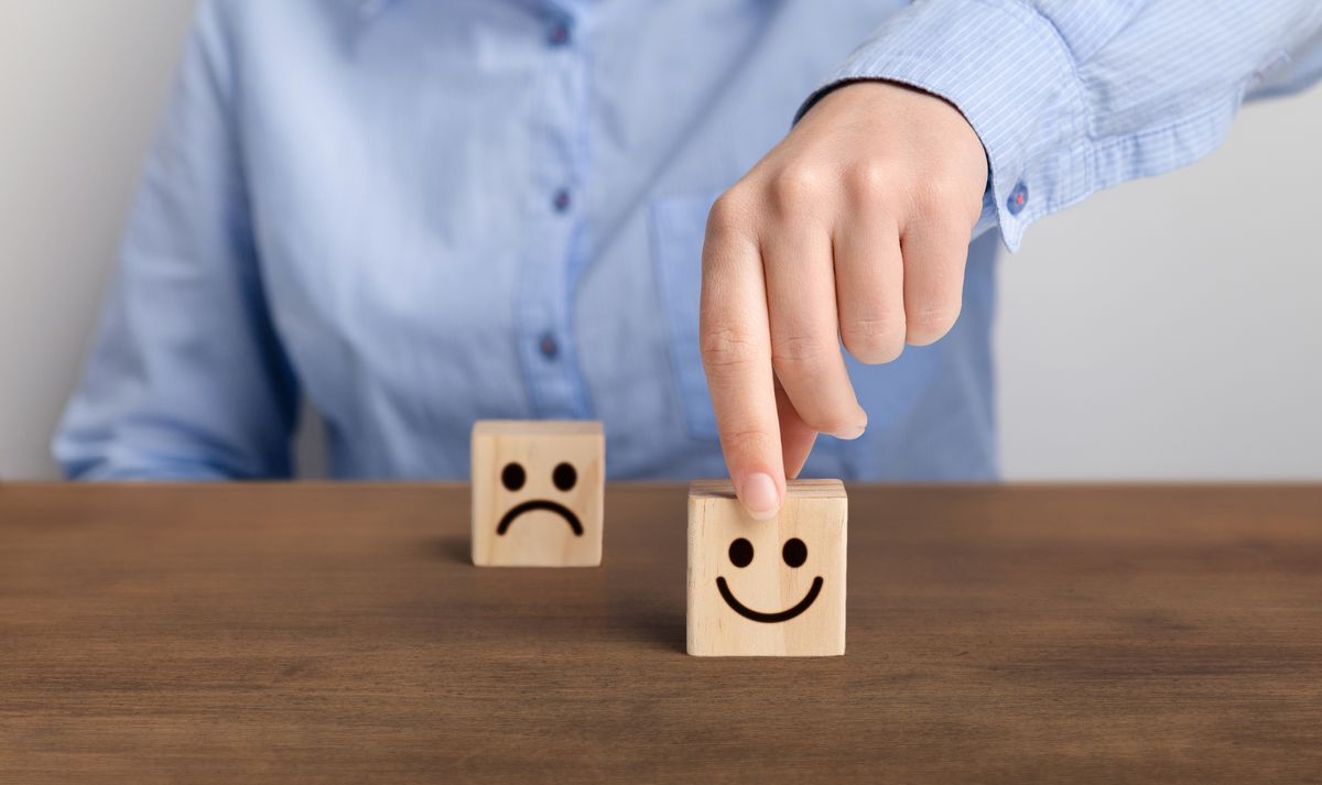 Two cubes with happy and sad faces. A person is touching the first one.
