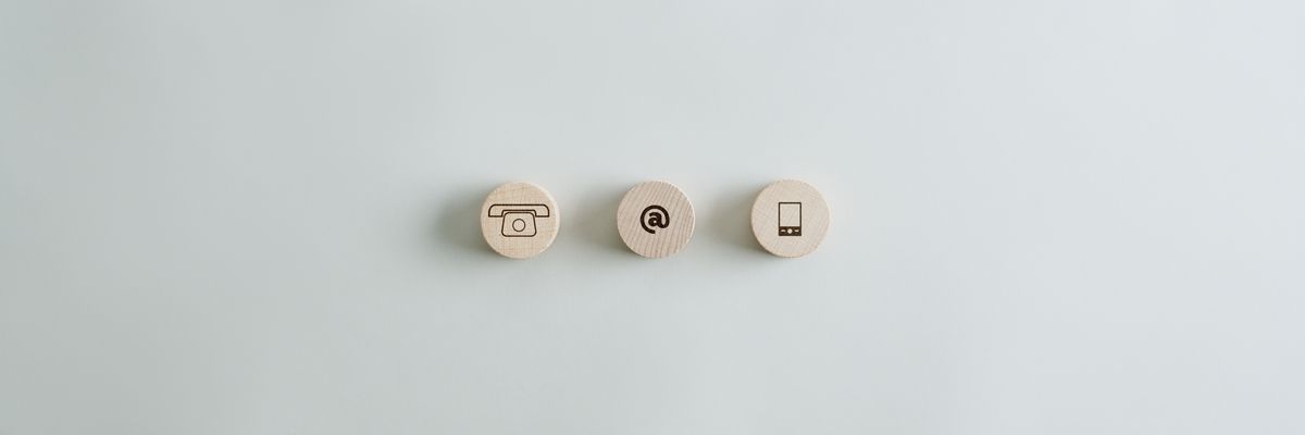 Na szarym tle leżą 3 drewniane kółka z symbolami: telefonu, e-maila (małpa) i smartfona.
